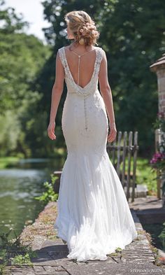 a woman in a wedding dress is walking down the path by water with her back to the camera