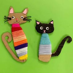 two cats made out of yarn sitting next to each other on a green surface with one cat wearing a colorful scarf