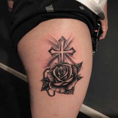 a cross and rose tattoo on the thigh