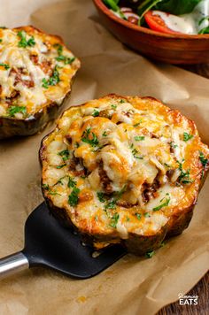 two stuffed potatoes with cheese and meat on top are sitting on wax paper next to a bowl of salad