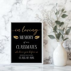 a black and gold memorial sign next to a white vase with greenery in it