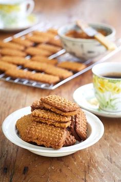 some cookies are stacked on a plate next to a cup of coffee and a tray of saucers