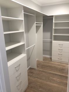 an empty walk in closet with white drawers and shelves on each side, along with wooden flooring