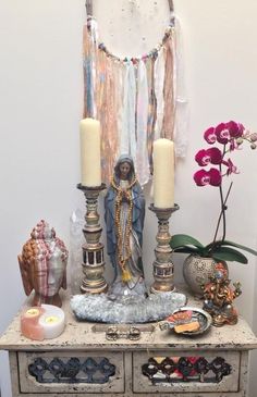 a table topped with candles and other items on it's side stand next to a wall hanging