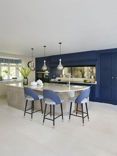 a large kitchen with blue cabinets and white counter tops, along with bar stools