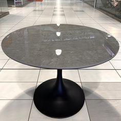 a round table sitting on top of a white tile floor in an empty room with no one around it