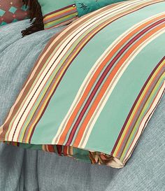 a bed with blue and green striped sheets, pillows and blankets on top of it