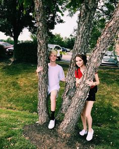 two young women standing next to each other near trees