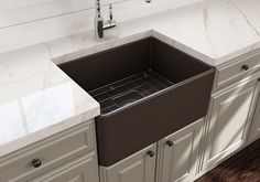 a kitchen sink with marble counter tops and white cupboards in the backround