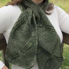 a woman wearing a green knitted scarf on top of a wooden bench in the grass