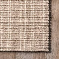 a beige rug on top of a wooden floor next to a white and brown wall