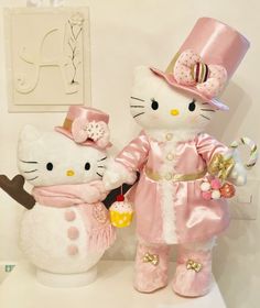 two hello kitty stuffed animals dressed in pink and gold outfits, standing next to each other