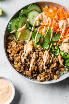 a white bowl filled with meat and veggies on top of rice next to dipping sauce