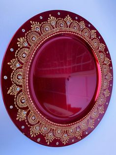 a red plate with gold designs on the rim and bottom, sitting against a white wall