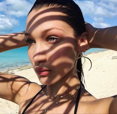 a woman standing on top of a beach next to the ocean with her hands behind her head