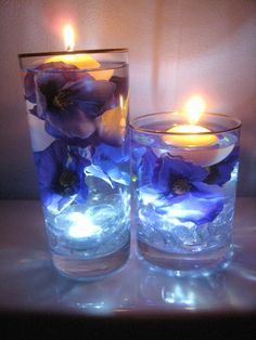 two glass vases filled with blue flowers and lit candles