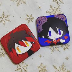 two square magnets with cartoon faces on them sitting on a white cloth covered surface