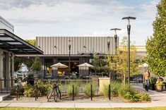 an outdoor cafe with tables and umbrellas on the side of the building, along with two people walking by