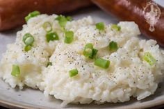 mashed potatoes and green onions on a plate with a hot dog in the background