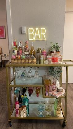 a bar cart filled with lots of bottles and glasses next to a neon sign that says bar