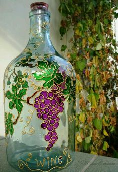 a glass bottle with some grapes painted on it's side and vines in the background