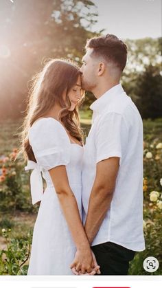 a man and woman standing next to each other in front of flowers with the sun behind them