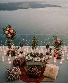 an outdoor table with candles and flowers on it, surrounded by other tables set up in front of the water