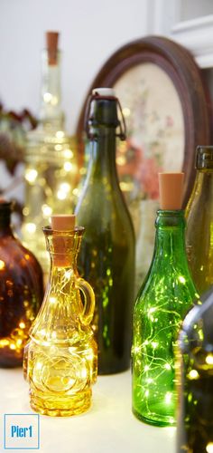 there are many different colored glass bottles on the table with string lights in front of them