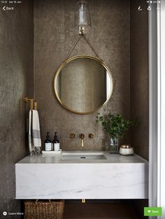 a white sink sitting under a mirror next to a wooden shelf with a potted plant