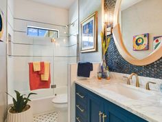 a bathroom with blue cabinets and white counter tops, gold accents on the mirror above the sink