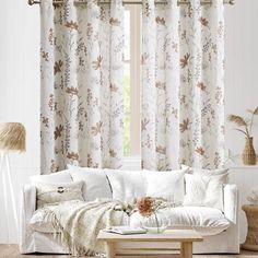 a living room filled with white furniture and curtains on the window sill, next to a coffee table