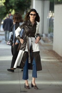 a woman in black and white coat walking down the street with her hand on her hip