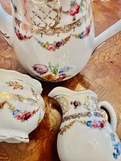 three pieces of porcelain sitting on top of a wooden table next to a glass pitcher