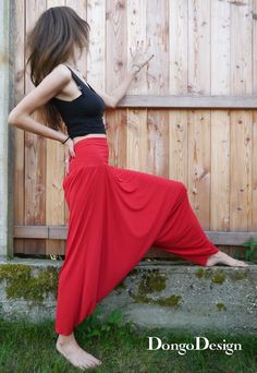 a woman leaning against a wooden fence wearing a red skirt