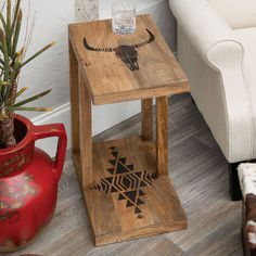 a wooden side table with a cow skull on it next to a red potted plant