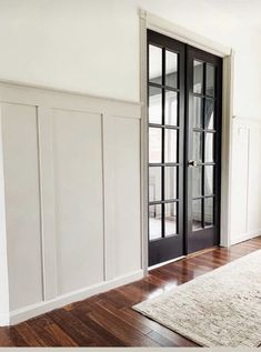 an empty room with white walls and black doors, hardwood floors, and a rug on the floor