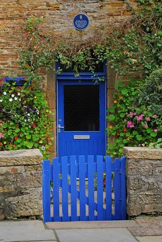 a blue gate is in front of a brick building with flowers growing on the wall