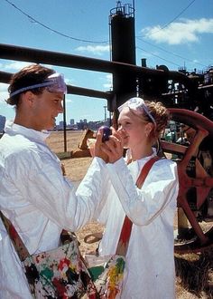 two people standing next to each other in front of a metal structure holding cell phones