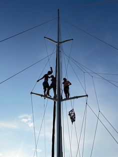 two people are standing on the top of a pole while another person is hanging from it