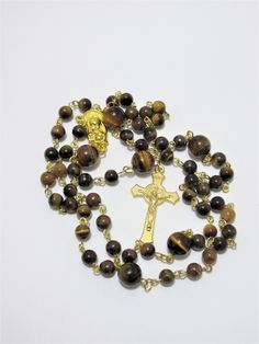 "This Tiger's eye Catholic rosary is made with Grade a gemstones. The hand turned links are gold plated as is the connector. The golden cross is from Italy. The rosary measures 26\" in the body and has a 5\" cross drop. This rosary will be slipped into a velvet bag and shipped in a bubble mailer." Gold Rosary Bracelet With Cross And 8mm Beads, Spiritual Gold Rosary With 8mm Beads, Gold Spiritual Rosary Bracelet With Polished Beads, Spiritual Yellow Gold Rosary With Round Beads, Brown Crucifix Necklace In Spiritual Style, Yellow Gold Rosary With Round Beads, Spiritual Brown Crucifix Necklace, Gold Spiritual Rosary With Round Beads, Gold Spiritual Rosary With Cross