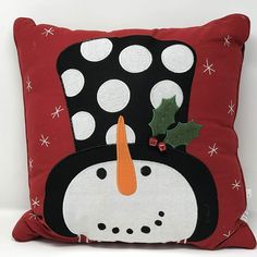 a red pillow with a black and white snowman wearing a holly berry hat on it