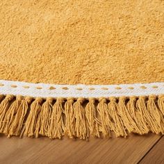 a close up of a yellow rug with fringes on the floor and wood floors