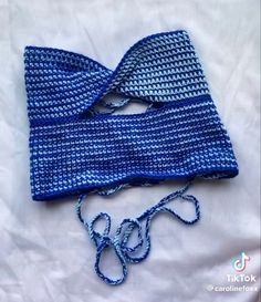 two pieces of blue crocheted fabric are laying on a white sheet and tied together