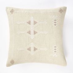 a white pillow with an embroidered design on the front and back, sitting against a white wall