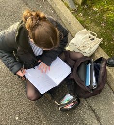 a woman is sitting on the curb with her backpack and papers in front of her