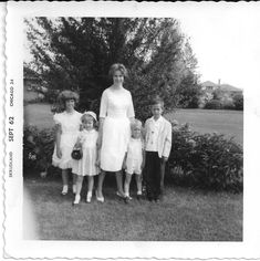 an old black and white photo of a woman standing with two children in front of bushes