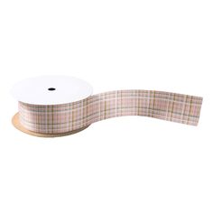 a roll of pink and green plaid ribbon on a wooden spooled edge with a white