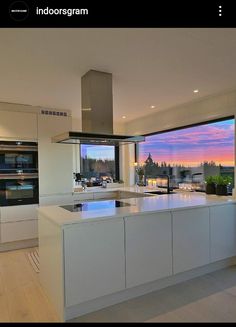 a large kitchen with an island counter top next to a window overlooking the water at sunset