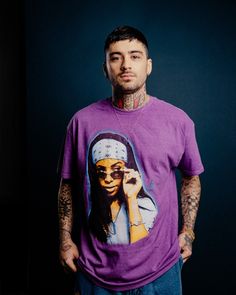 a man with tattoos standing in front of a black background wearing a purple shirt and blue jeans