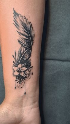 a woman's arm with a feather and flower tattoo on the left side of her wrist